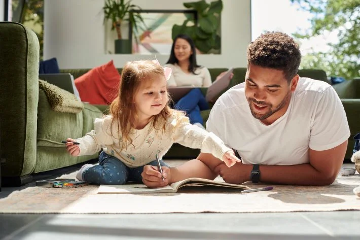 A father spending quality time with his daughter while the mother smiles in the background.