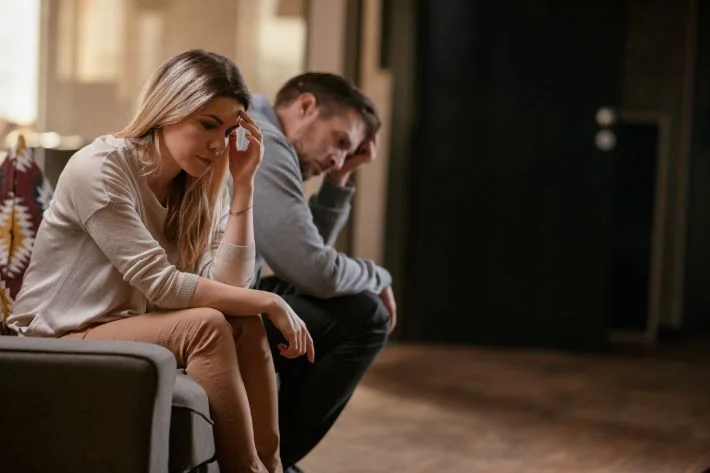 An unhappy couple sat on sofa, turned away from each other.