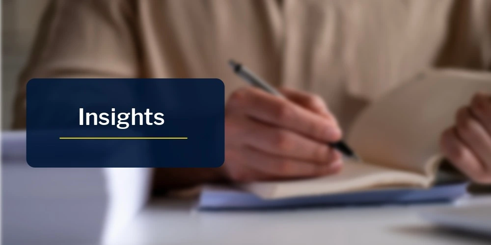 Blurred close-up of a person writing notes in an open notebook at a desk, with a blue overlay panel displaying the word 'Insights'