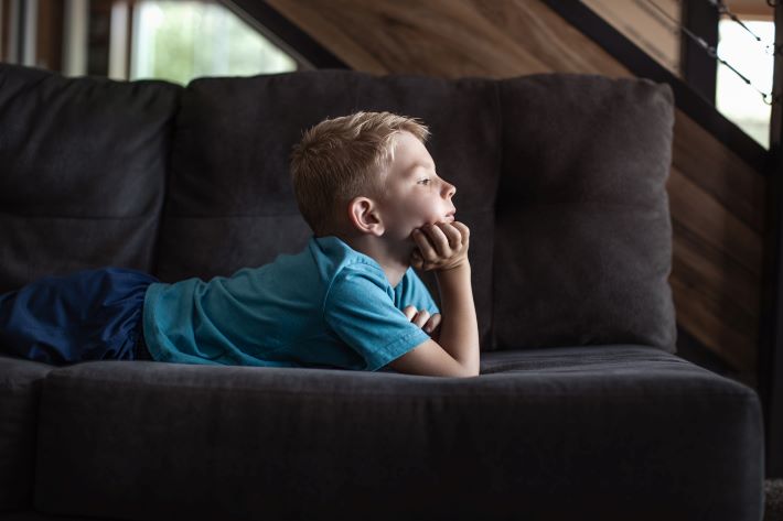 Boy relaxing on the sofa at home, gazing out of the window