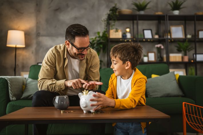 Father showing son how to save money in a piggy bank at home.