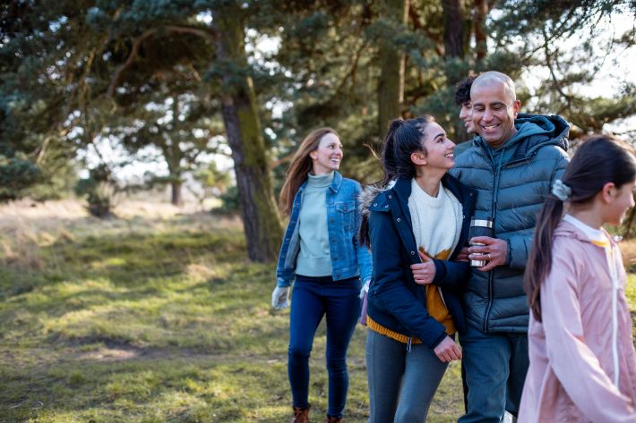 Father and teenage daughter embrace as family walks through countryside.