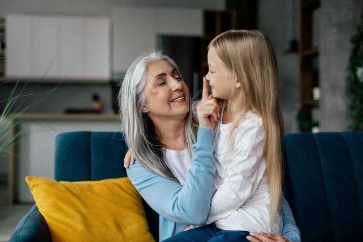 A loving grandparent hugs her small granddaughter and gently touches her nose.