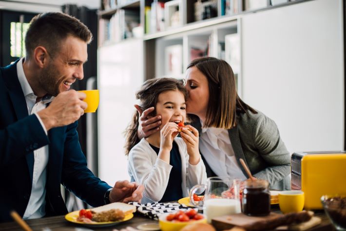Young couple and their daughter having a breakfast together at home before work.