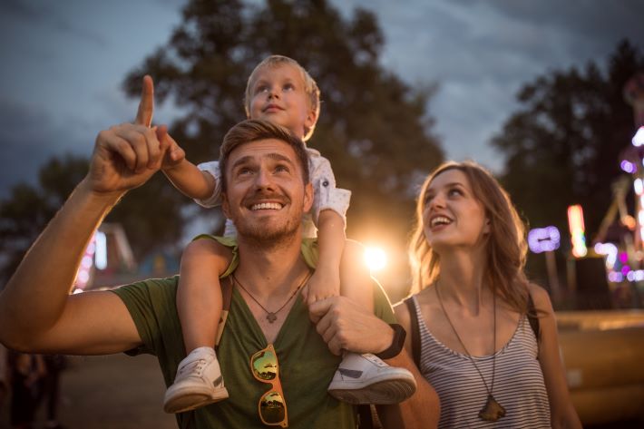 Family with one child outdoors on summer event. Father carrying son on shoulders.