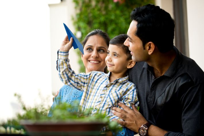 Happy parents with son throwing paper airplane in air.