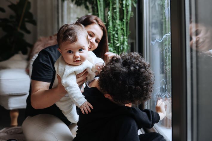 Young happy children hugging their mother at home, while looking out of the window.