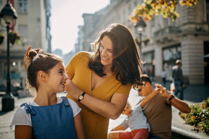 Mother doing daughters hair while father and son play in the background.