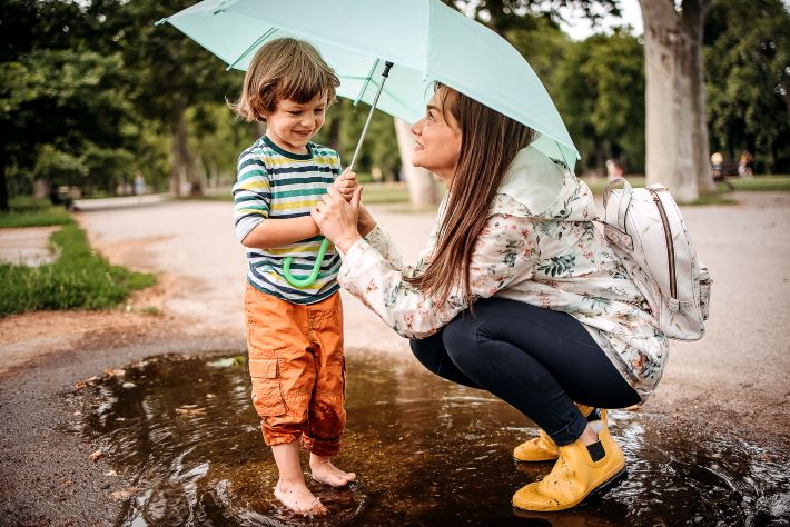 A mother and son playing in the rain with an umbrella in the park.