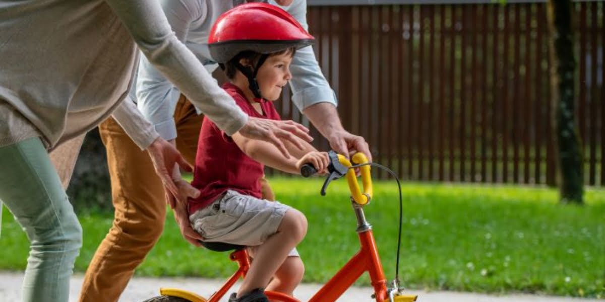 A child learning to ride a bike with parents supporting.